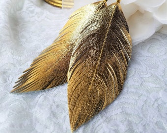 May include: Gold feather earrings with a textured finish. The earrings are dangle style and have a hook closure.