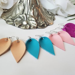 May include: Six pairs of leather earrings in various colors, including pink, teal, and brown. Each earring is shaped like a teardrop and hangs from a silver hook.