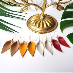 May include: Six pairs of leather earrings in various colors, including beige, yellow, white, and red. The earrings are shaped like a leaf and have a gold hook.