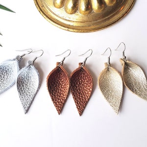 May include: Three pairs of dangle earrings with silver, gold, and copper leaf-shaped charms. The earrings are made of leather and have a simple, elegant design.