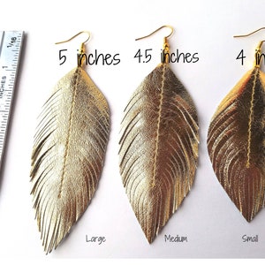 May include: Three pairs of gold leather feather earrings in different sizes: 5 inches, 4.5 inches, and 4 inches. The earrings are labeled "Large", "Medium", and "Small".
