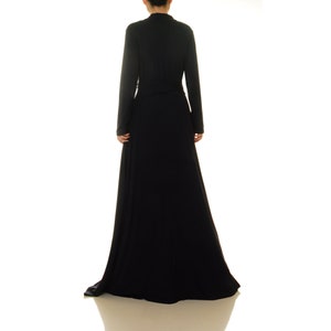 K&ouml;nnte beinhalten: Ein langes schwarzes Maxikleid mit V-Ausschnitt und langen &Auml;rmeln. Das Kleid hat einen Wickelstil und einen Bindeg&uuml;rtel in der Taille.