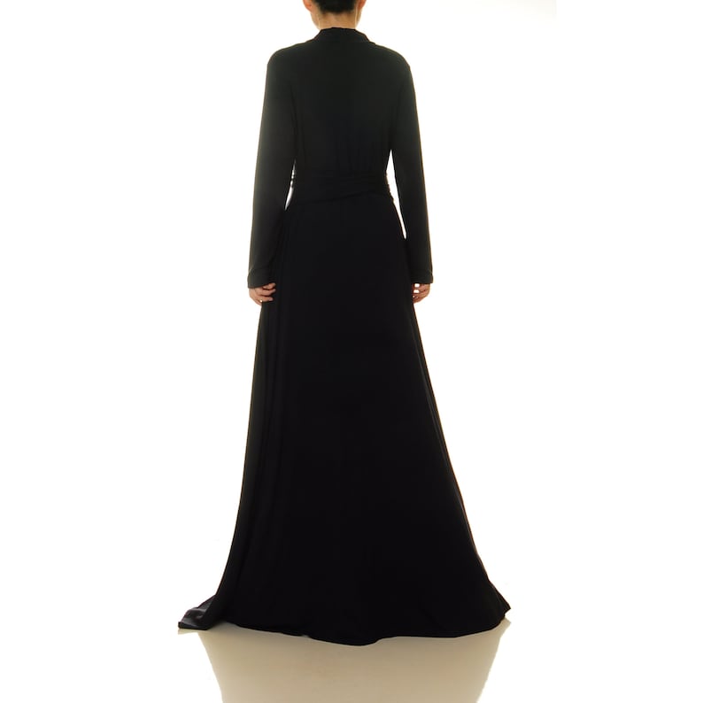 K&ouml;nnte beinhalten: Ein langes schwarzes Maxikleid mit V-Ausschnitt und langen &Auml;rmeln. Das Kleid hat einen Wickelstil und einen Bindeg&uuml;rtel in der Taille.