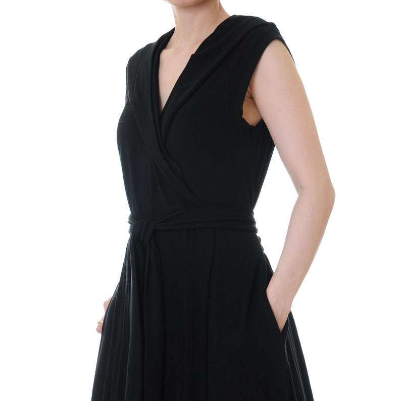 May include: A black wrap dress with a V-neckline and short sleeves. The dress has a tie at the waist and a flowing skirt.