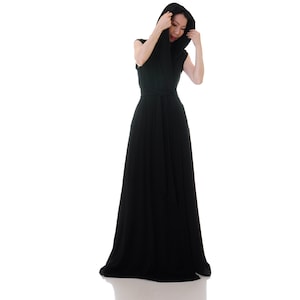 May include: A woman wearing a long, black maxi dress with a hood. The dress has a wrap style and a belt at the waist.