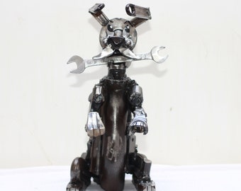 May include: A metal sculpture of a dog made from recycled parts, such as wrenches and gears. The dog is sitting with its front paws raised and has a wrench for a mouth.