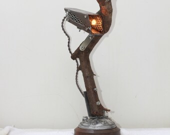 May include: A unique table lamp made from a natural branch with a metal light fixture. The lamp has a warm, ambient glow and a rustic, industrial design.