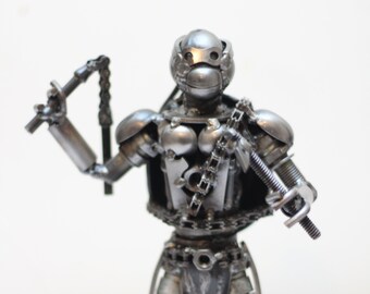 May include: A silver metal sculpture of a Teenage Mutant Ninja Turtle holding a sai and a chain. The sculpture is made of recycled metal parts and is a unique and detailed piece of art.