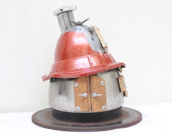 May include: A small, red and silver metal house sculpture with a chimney and a wooden door. The house is sitting on a round, black metal base.