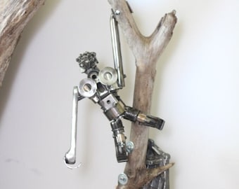 May include: A metal sculpture of a figure climbing a tree branch. The sculpture is made of recycled metal parts, including gears, bolts, and nuts. The tree branch is made of driftwood. The sculpture is mounted on a metal base.