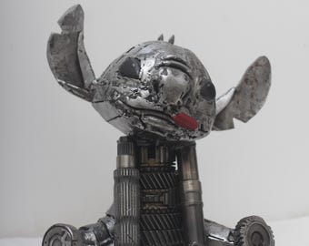 May include: A metal sculpture of a cartoon character, Stitch from Lilo & Stitch, made from recycled metal parts. The sculpture is in a sitting position with its arms and legs made from gears and other metal pieces.