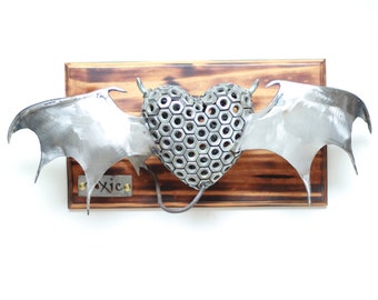 May include: A metal sculpture of a heart with wings. The heart is made of hexagonal nuts and the wings are made of metal. The sculpture is mounted on a wooden plaque with the word "Toxic" written on it.
