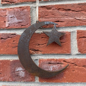 May include: A rusty metal crescent moon and star ornament hanging from a string. The ornament is a popular symbol of Islam and is often used as a decoration during Ramadan.