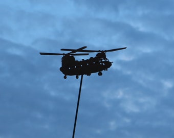 May include: A black silhouette of a helicopter against a blue sky. The helicopter is mounted on a thin metal pole.
