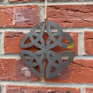 May include: A rustic metal ornament in the shape of a Celtic knot. The ornament is a dark grey colour with a hint of rust and has a distressed finish. It is hanging from a string.