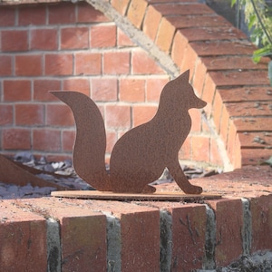 May include: A rusty metal silhouette of a fox, standing on a brick wall. The fox is facing to the right and has a long, bushy tail.
