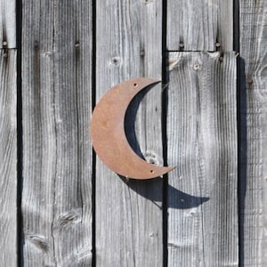 May include: A rusty metal crescent moon shape is attached to a weathered wooden wall.