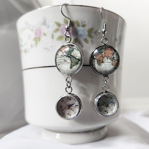May include: A pair of silver earrings with a compass and a globe design. The globe is a vintage map with brown, green, and blue colors. The compass is silver with a black needle and a white face with black markings.