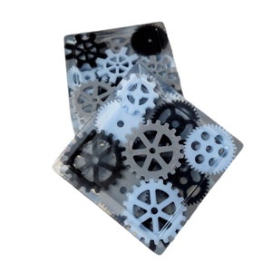 May include: Two clear resin square coasters with embedded gears in black, gray, and light blue.
