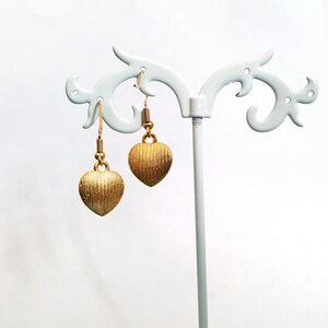 May include: A pair of gold heart-shaped earrings hanging on a white display stand.