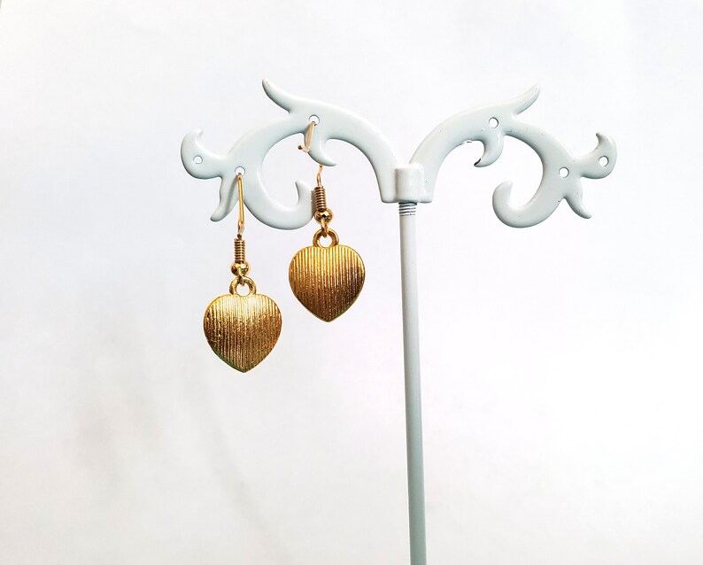 May include: A pair of gold heart-shaped earrings hanging on a white display stand.