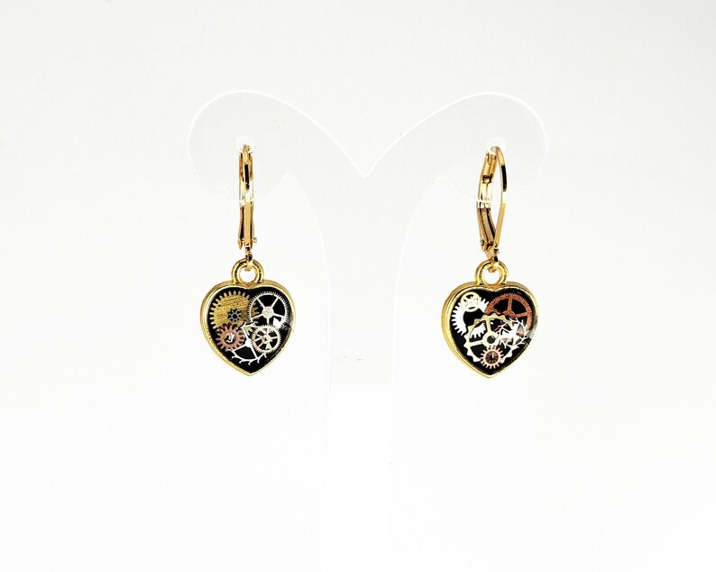 May include: A pair of gold-tone earrings with a black heart-shaped charm featuring a detailed design of gears and cogs.
