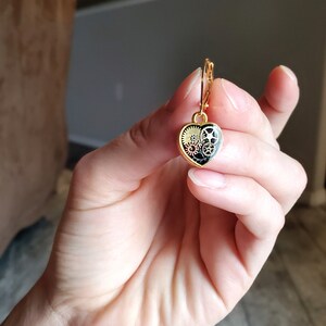 May include: Gold heart-shaped earring with a black and gold gear design.