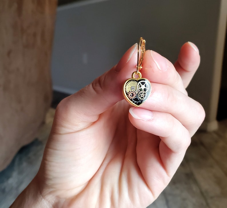 May include: Gold heart-shaped earring with a black and gold gear design.