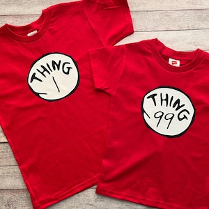 May include: Two red t-shirts with a white circle and black text that says "Thing 1" and "Thing 99".