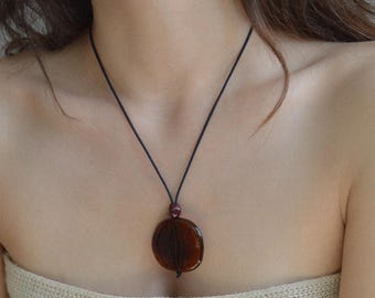 May include: A dark brown pendant necklace with a circular, translucent design. The pendant hangs from a thin, black cord. The necklace is a simple, elegant piece of jewelry.