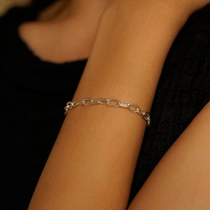 May include: A silver chain bracelet on a person's wrist.