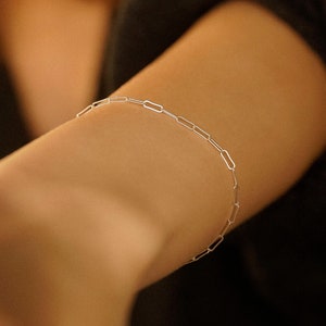 Può includere: Un braccialetto a catena d'argento con un design delicato e collegato. Il braccialetto è indossato al polso.