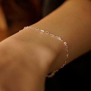 May include: A delicate silver chain bracelet with oval-shaped links. The bracelet is on a person's wrist.
