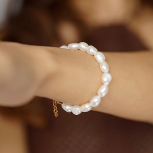 May include: A white pearl bracelet with a gold chain clasp. The bracelet is made of a string of round, white pearls.