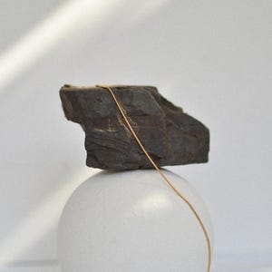 May include: A gold chain necklace draped over a dark grey rock, which is balanced on top of a white sphere.