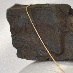 May include: A gold chain necklace on a dark grey rock.