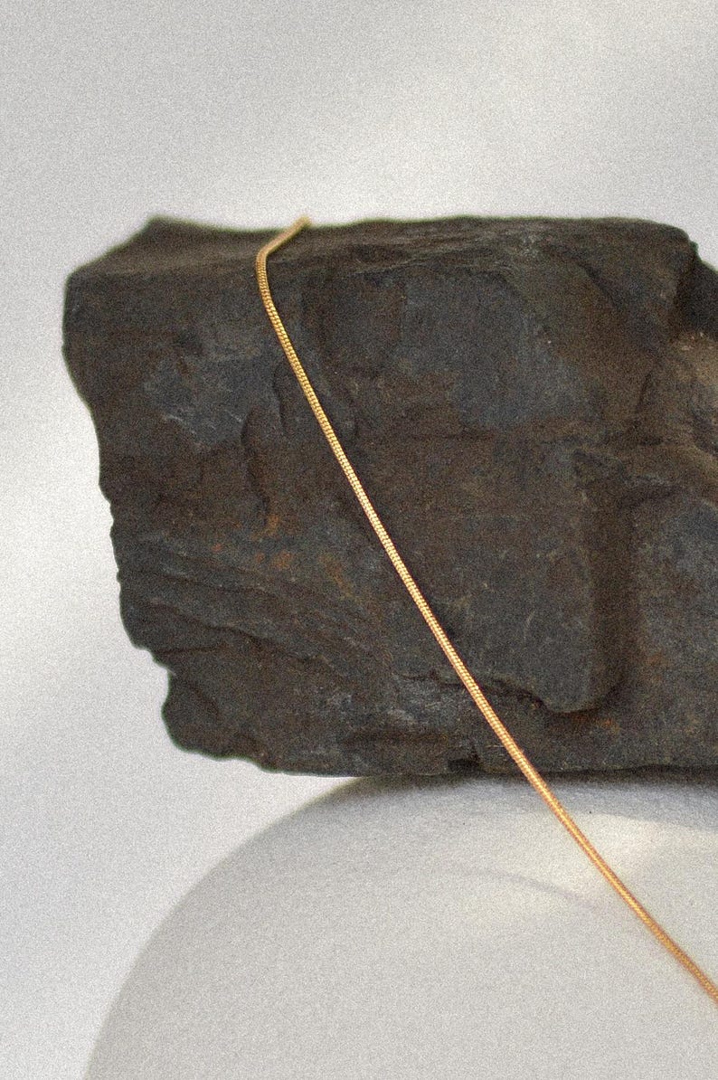 May include: A gold chain necklace on a dark grey rock.