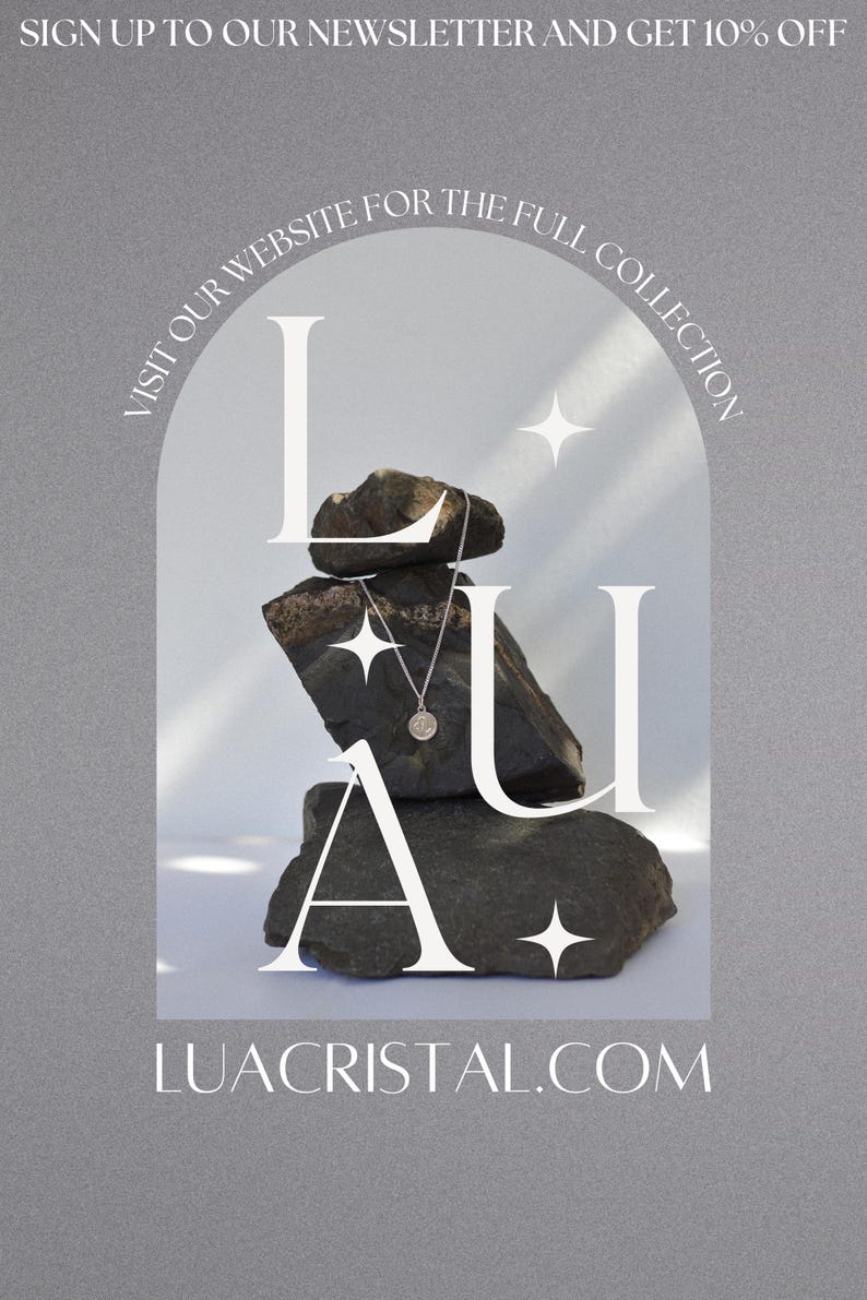 May include: A silver necklace with a circular pendant is displayed on a stack of dark gray stones. The word "LUA" is superimposed in white over the stones, with the website address LUACRISTAL.COM at the bottom. The background is a light gray.