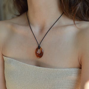 May include: A brown oval pendant necklace with a black cord. The pendant has a layered design and a glossy finish. The necklace is worn around the neck.