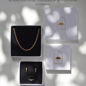 Op de afbeelding: Sieradenpresentatie met een gouden ketting, oorbellen en een ring in zwart gevoerde dozen. Deze bevinden zich in witte geschenkdozen met de tekst "LUA CRISTAL". De afbeelding bevat ook tekst over duurzame verpakkingen.
