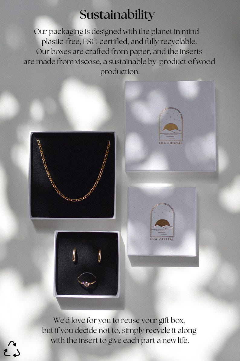 Op de afbeelding: Sieradenpresentatie met een gouden ketting, oorbellen en een ring in zwart gevoerde dozen. Deze bevinden zich in witte geschenkdozen met de tekst "LUA CRISTAL". De afbeelding bevat ook tekst over duurzame verpakkingen.