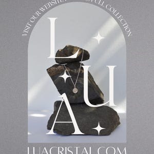 May include: A silver necklace with a small pendant charm sits on top of a stack of grey rocks. The necklace is displayed against a white background with the text "LUA" in white letters. The text "VISIT OUR WEBSITE FOR THE FULL COLLECTION" is written in a circle around the rocks. The text "LUACRISTAL.COM" is written below the rocks.