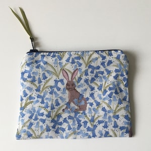 May include: A zipped pouch featuring a bluebell floral design and a brown rabbit illustration. The pouch has a green ribbon attached to the zipper. The background is white.