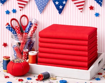 May include: A stack of eight folded red fabric squares sits on a white tray next to a glass jar filled with red, white, and blue patterned sewing tools, a red tomato-shaped pincushion, and scattered small star-shaped buttons and thread spools.