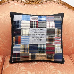 May include: A square throw pillow constructed from a patchwork of various plaid and checkered fabric squares in shades of blue, red, white, and grey. A central light grey panel features the embroidered text: This is a shirt I used to wear. Whenever you hold it, know I am there. Love, Papa.