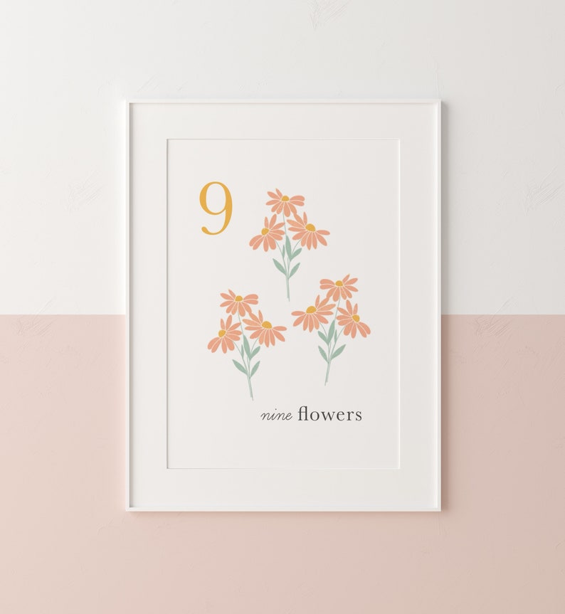 May include: A white framed print with a yellow number 9 and nine pink flowers with green stems. The text "nine flowers" is below the flowers.