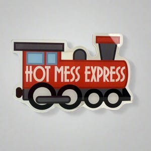 May include: A red and black train-shaped sticker with the words "HOT MESS EXPRESS" in white. The sticker has a clear, glossy finish and features blue windows and black wheels. The overall design is a playful, cartoon-like representation of a train.