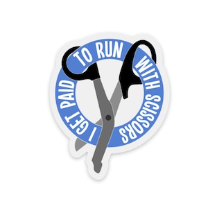 May include: A white sticker with a blue border and the text "I GET PAID TO RUN WITH SCISSORS" in white. The sticker features a pair of scissors in grey and black, with the text arranged in a circular pattern.
