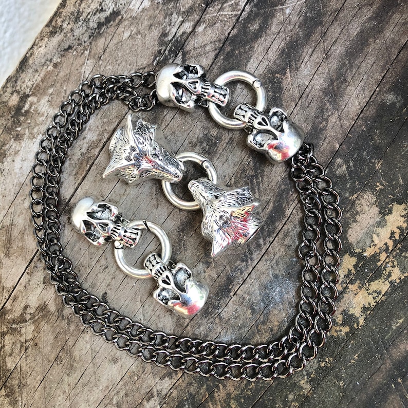 May include: A silver chain necklace with multiple charms, including wolf heads and skull designs. The chain is black and silver.
