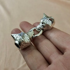 May include: Silver wolf head toggle clasp with a ring connecting two wolf heads. The heads are detailed with fur and have a realistic look.